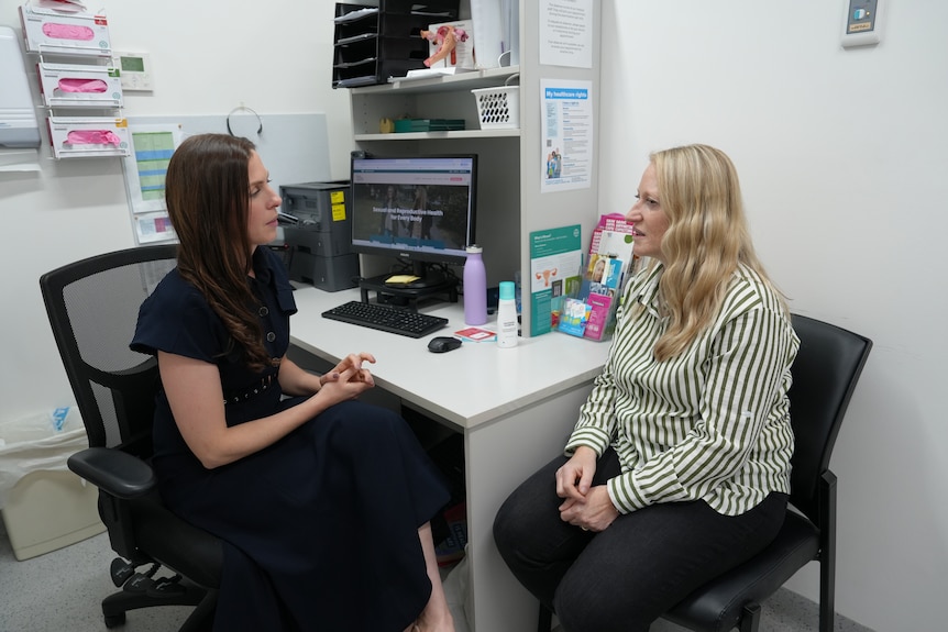 A female doctor speaks with a female patient in a consulting room.