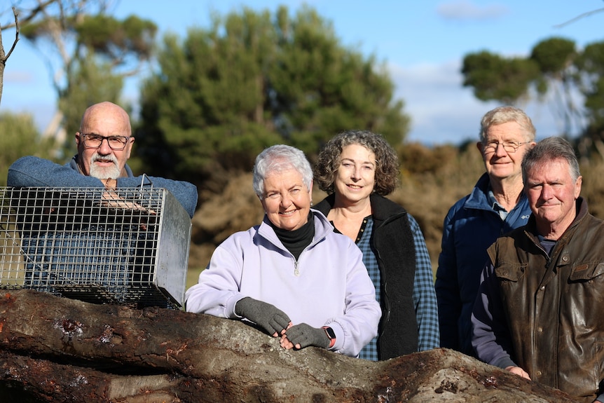 A man leans on a metal animal trap perched on a tree branch next to two women and two men