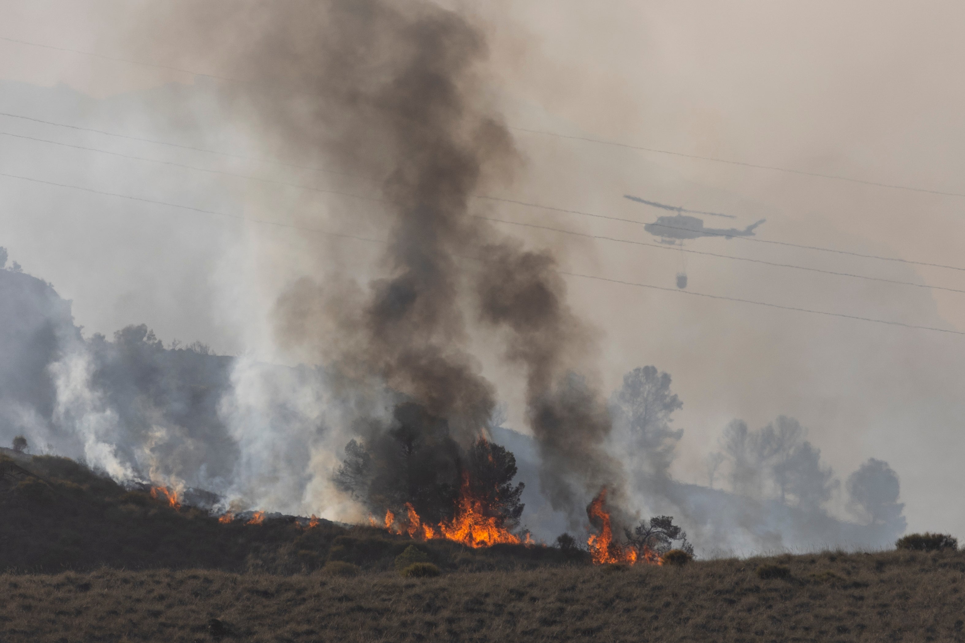 A helicopter drops water as flames and smoke rise from a wildfire near the municipality of Los Gallardos