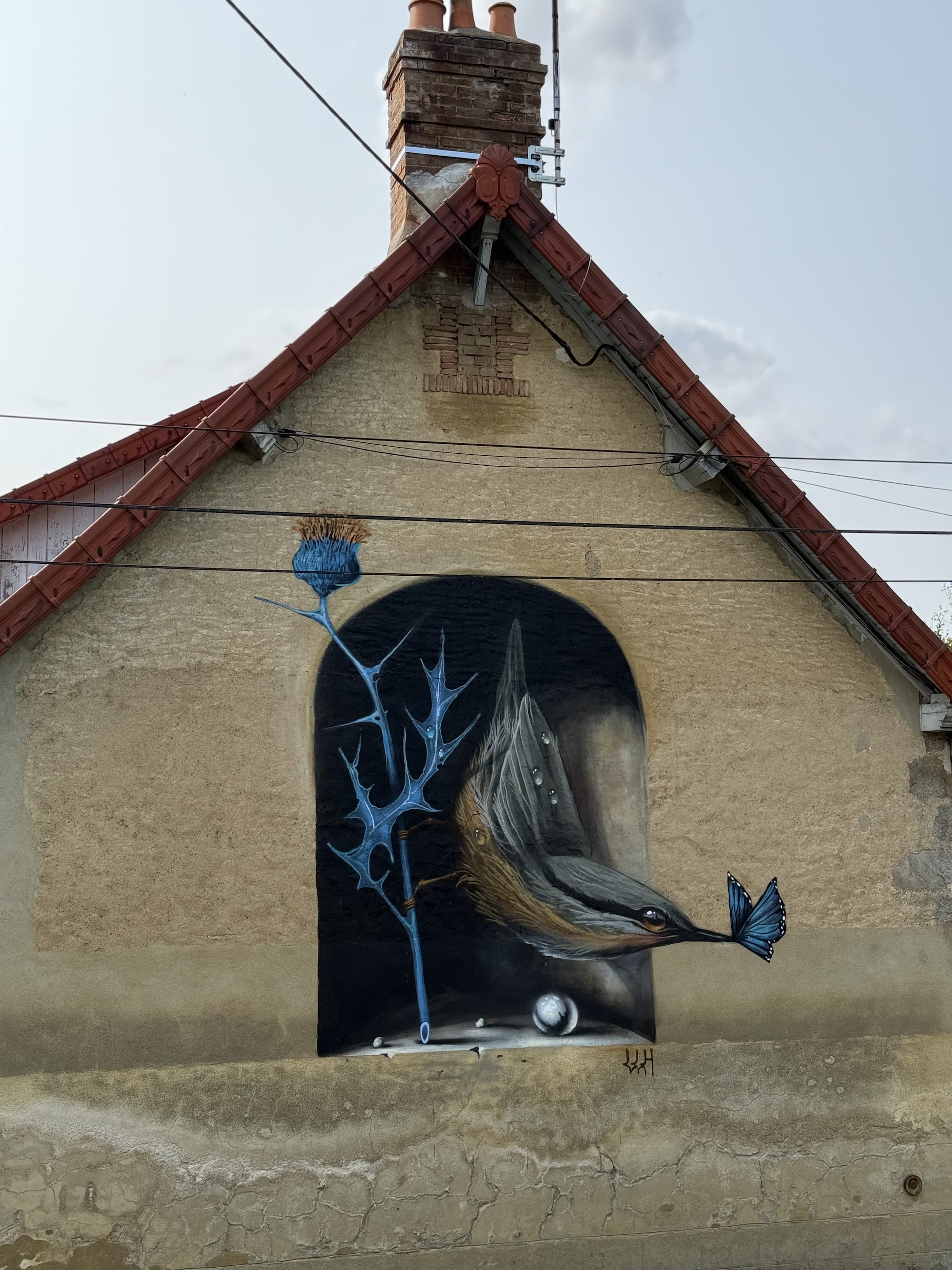 a small mural in the gable of a historic building depicting a bird and a thistle inside of a niche in the wall