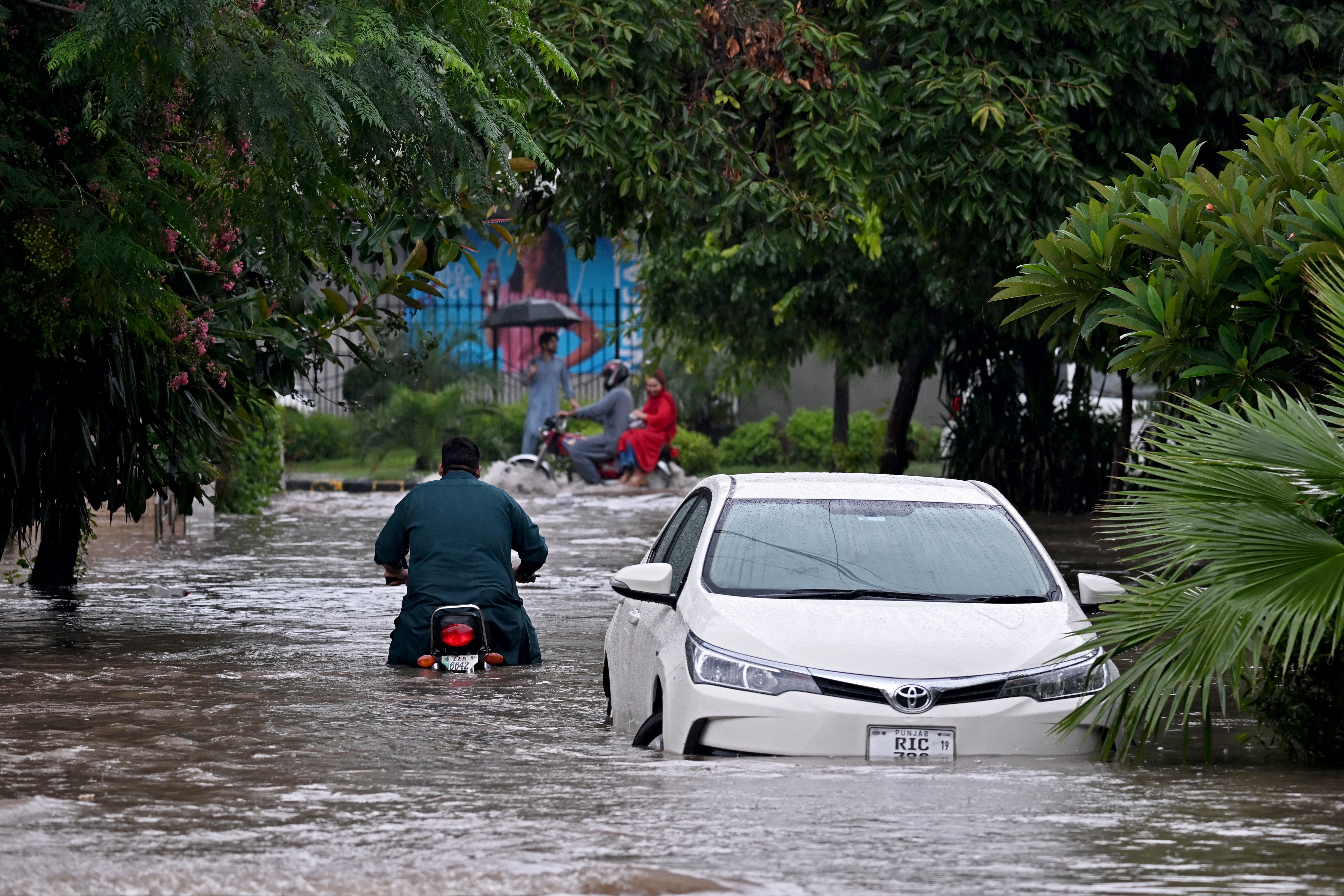 Commuters wade through a flooded street after heavy rainfall in Rawalpindi, Pakistan