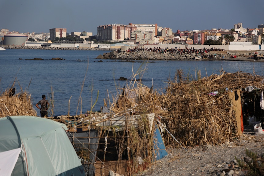 Tents and makeshift shelter in foregroud with crowd on seawall in background.