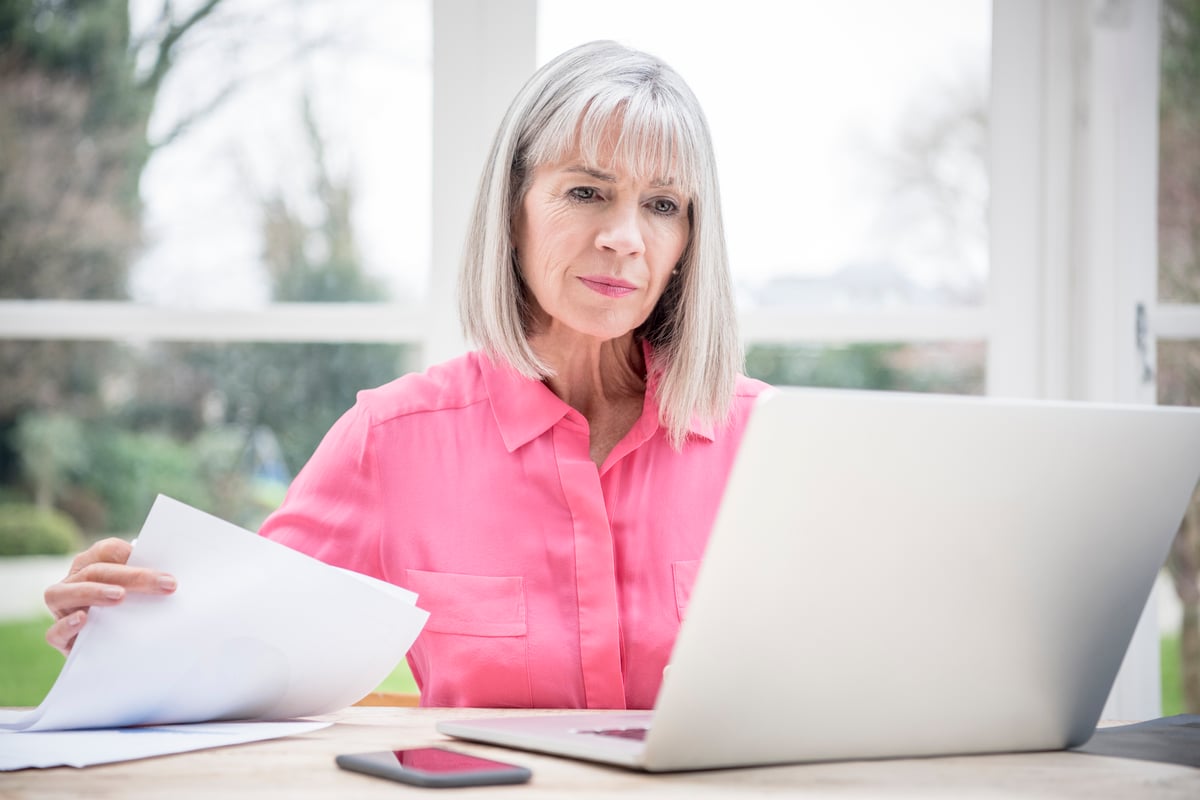 Person holding document and staring at laptop.