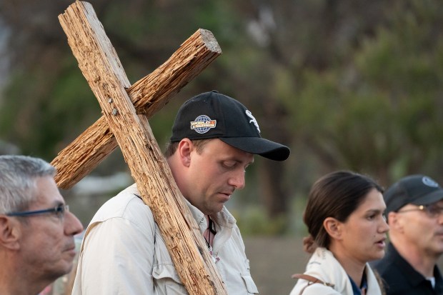 A man carries a large cross over his shoulder while...