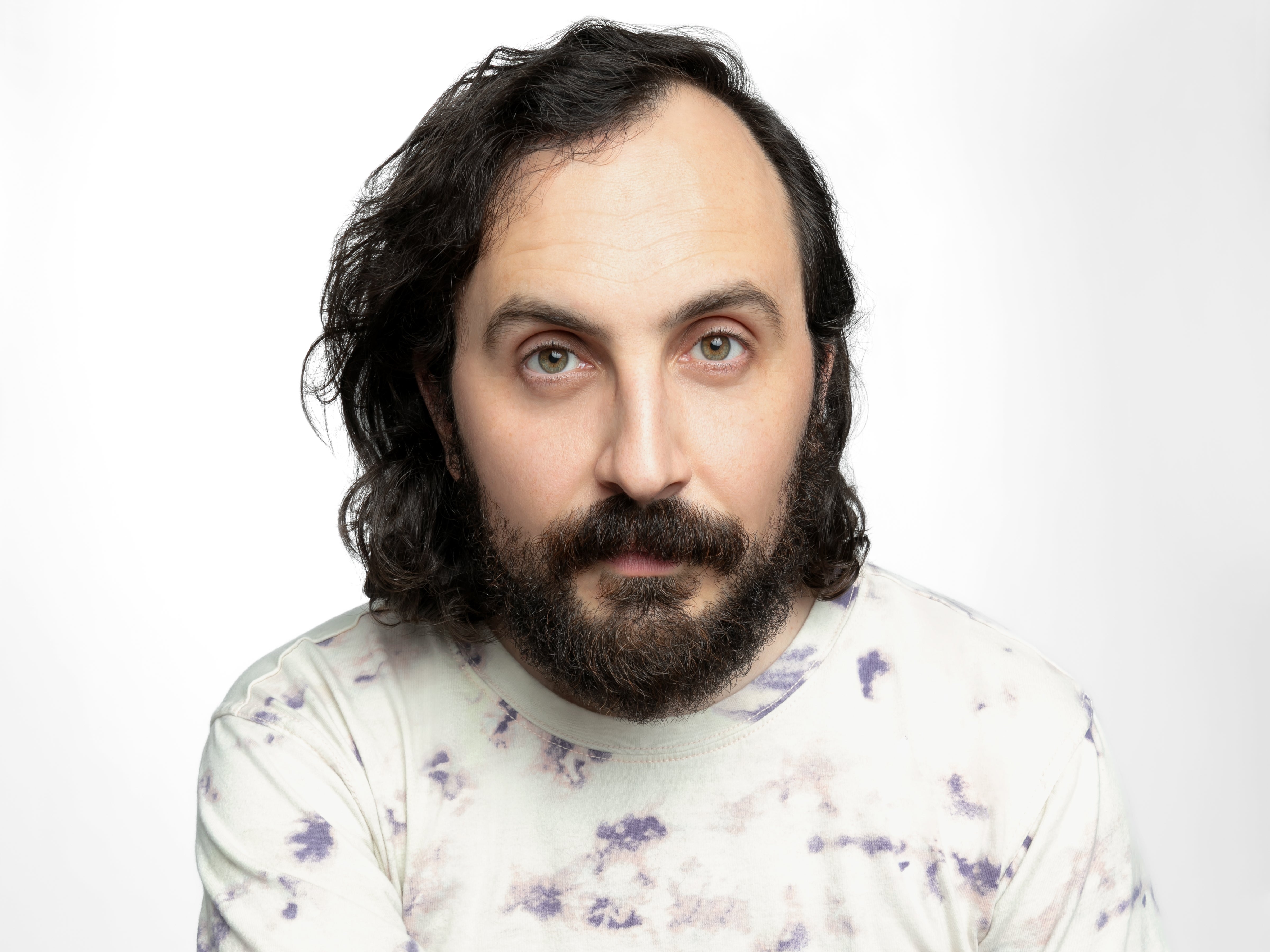 A middle-aged white person with shoulder-length dark wavy hair in a purple-and-white tie-dye T-shirt.