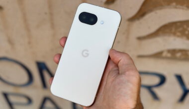 The Porcelain Google Pixel 9a held in hand in front of a tan sign.