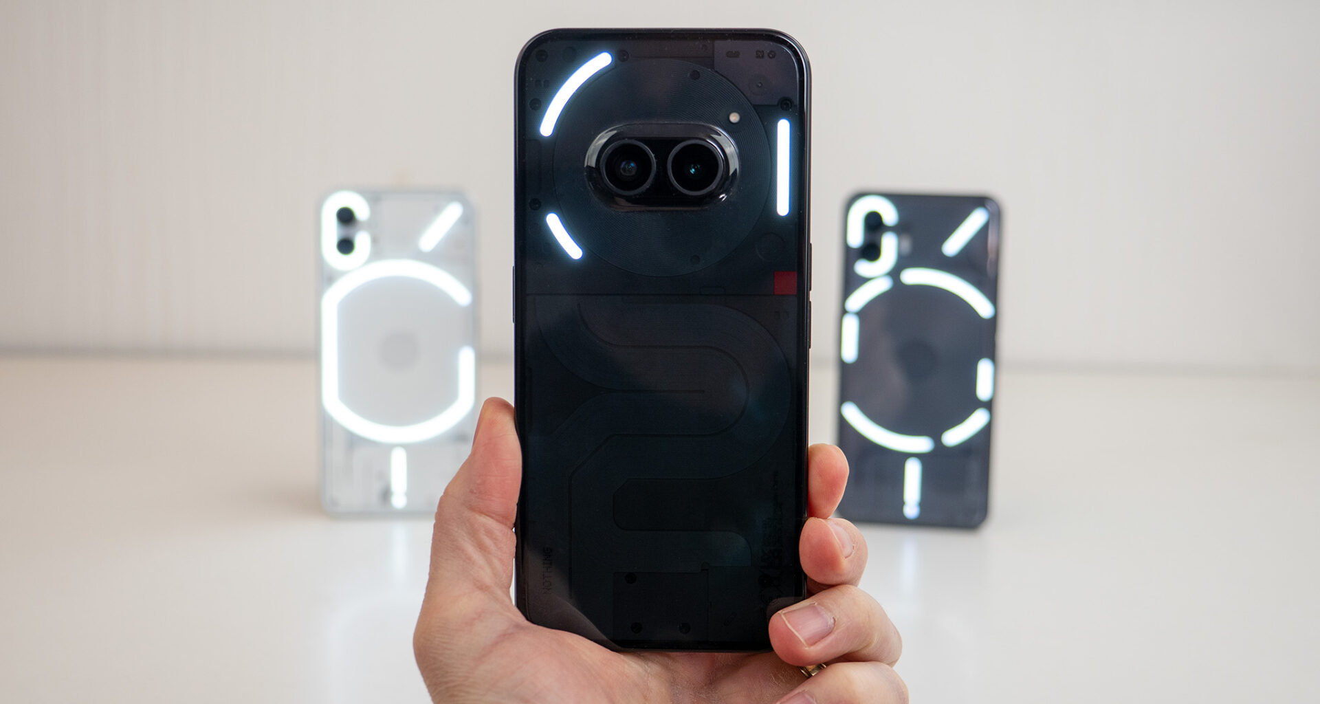 Holding the Nothing Phone (2a) with Nothing Phone (1) and Nothing Phone (2) in the background