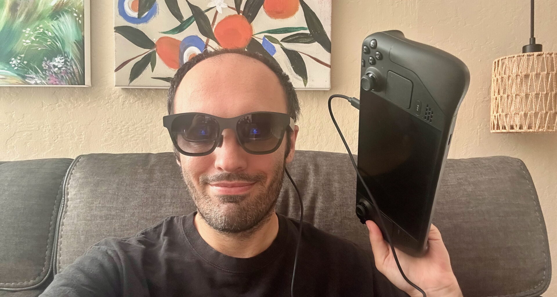 A selfie of the author wearing XREAL Air 2 AR glasses tethered to a Steam Deck held in his left hand next to his face.