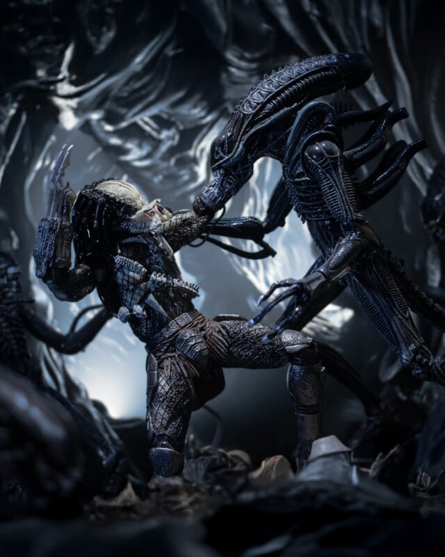 A detailed action figure scene of a Predator and an Alien locked in combat inside a dark, sci-fi cave setting, with dramatic lighting highlighting their fierce struggle.