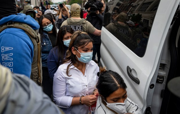 Handcuffed detainees are led into a van by federal agents on South Michigan Avenue as protesters demonstrate on June 4, 2025, outside the Intensive Supervision Appearance Program office run by Immigration and Customs Enforcement in the South Loop. (Brian Cassella/Chicago Tribune)