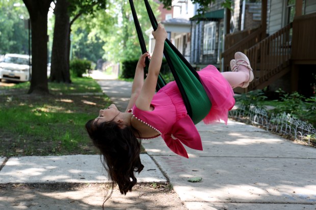 Following her kindergarten graduation, Gabriela Pineda, 6, takes a ride on a neighbor's swing outside her home in Chicago on June 11, 2025. (Antonio Perez/Chicago Tribune)