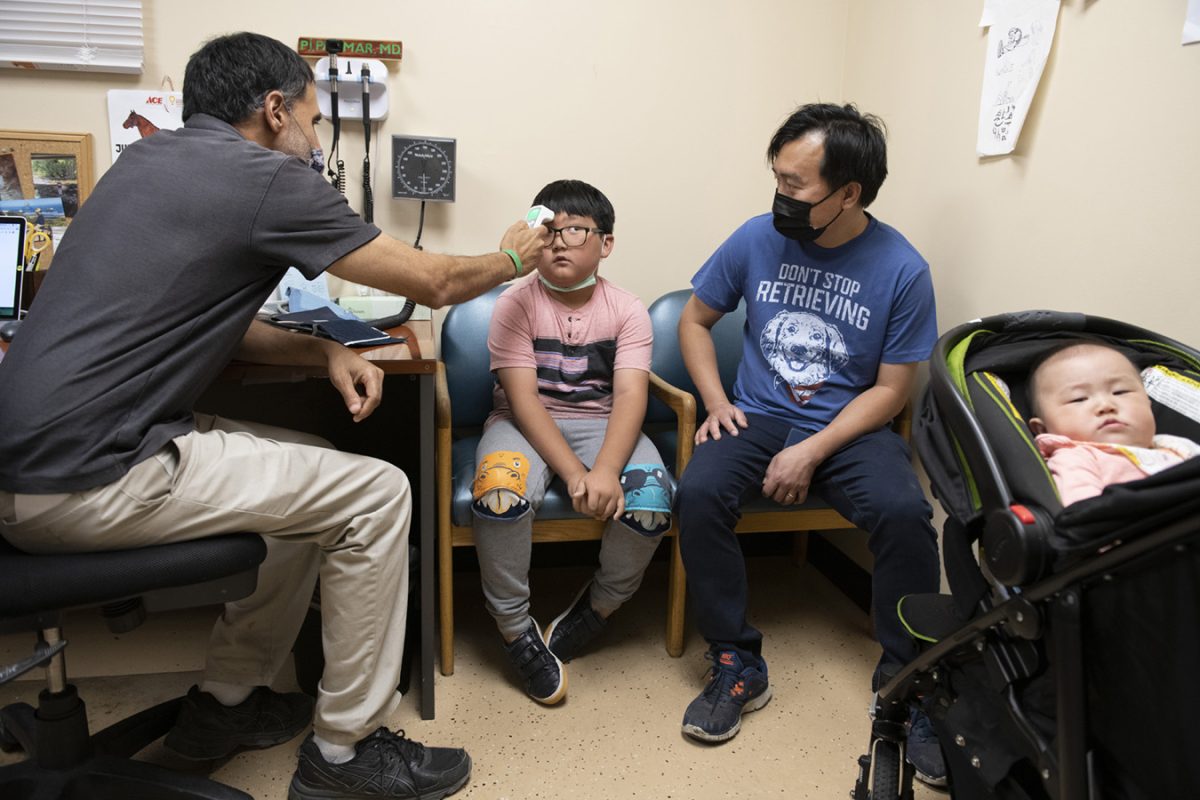 A doctor checks the temperature of a little boy while his dad watches