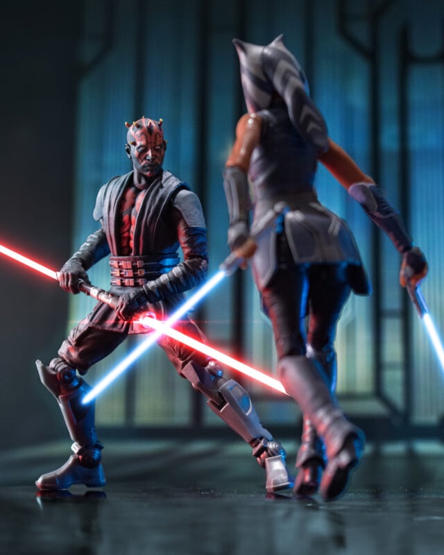 Two Star Wars action figures, Darth Maul with a double-bladed red lightsaber faces off against Ahsoka Tano, who wields two blue lightsabers, in a dramatic, futuristic setting.