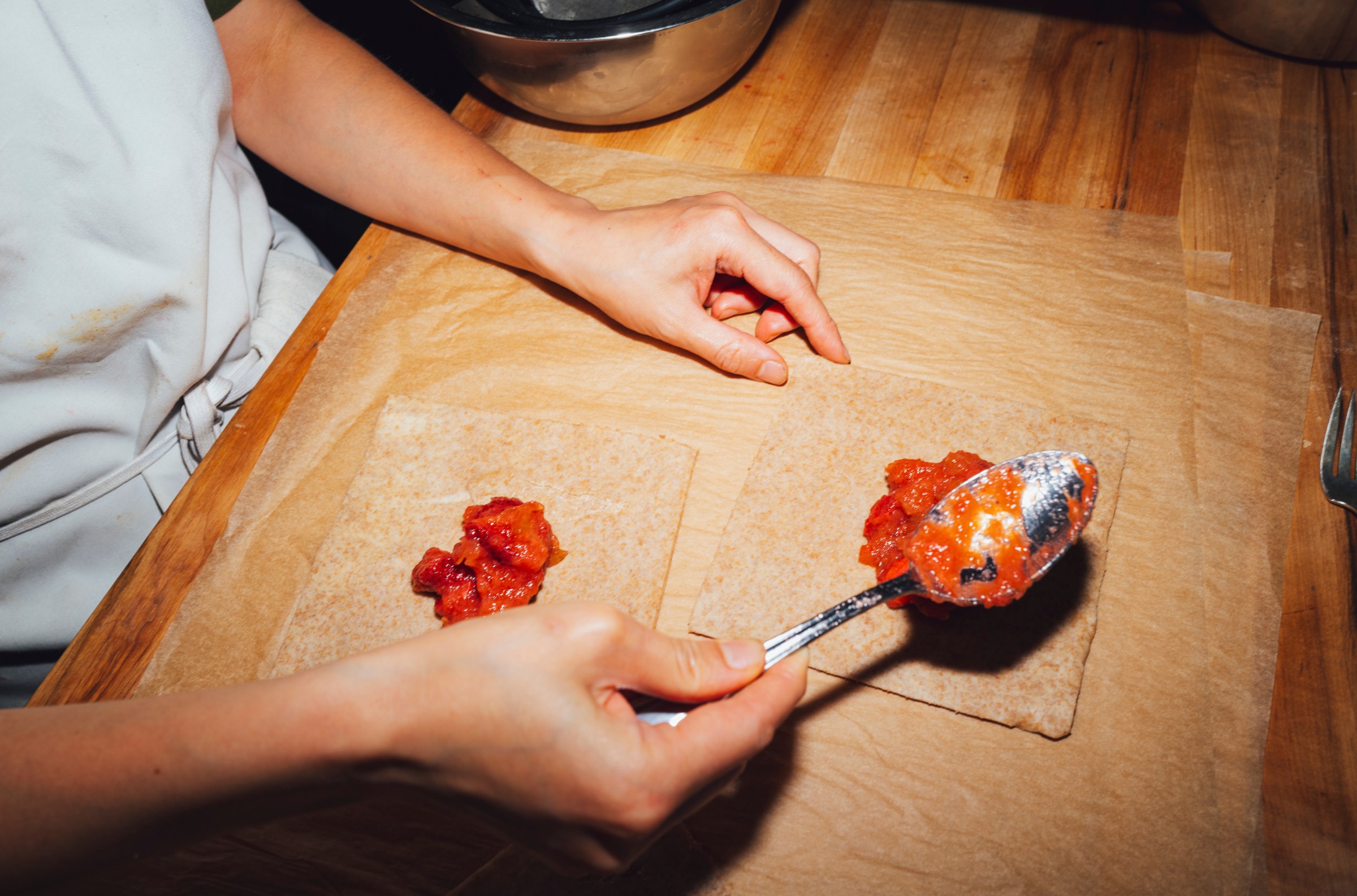 Someone spooning strawbrries onto flat doughs.