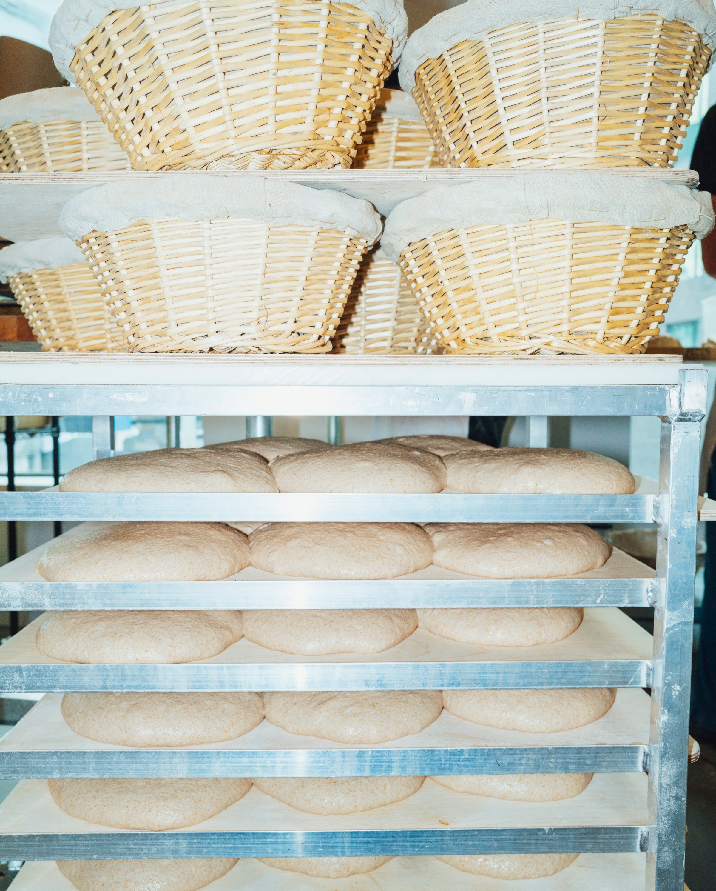 A shelf of doughs below a shelf of baskets.