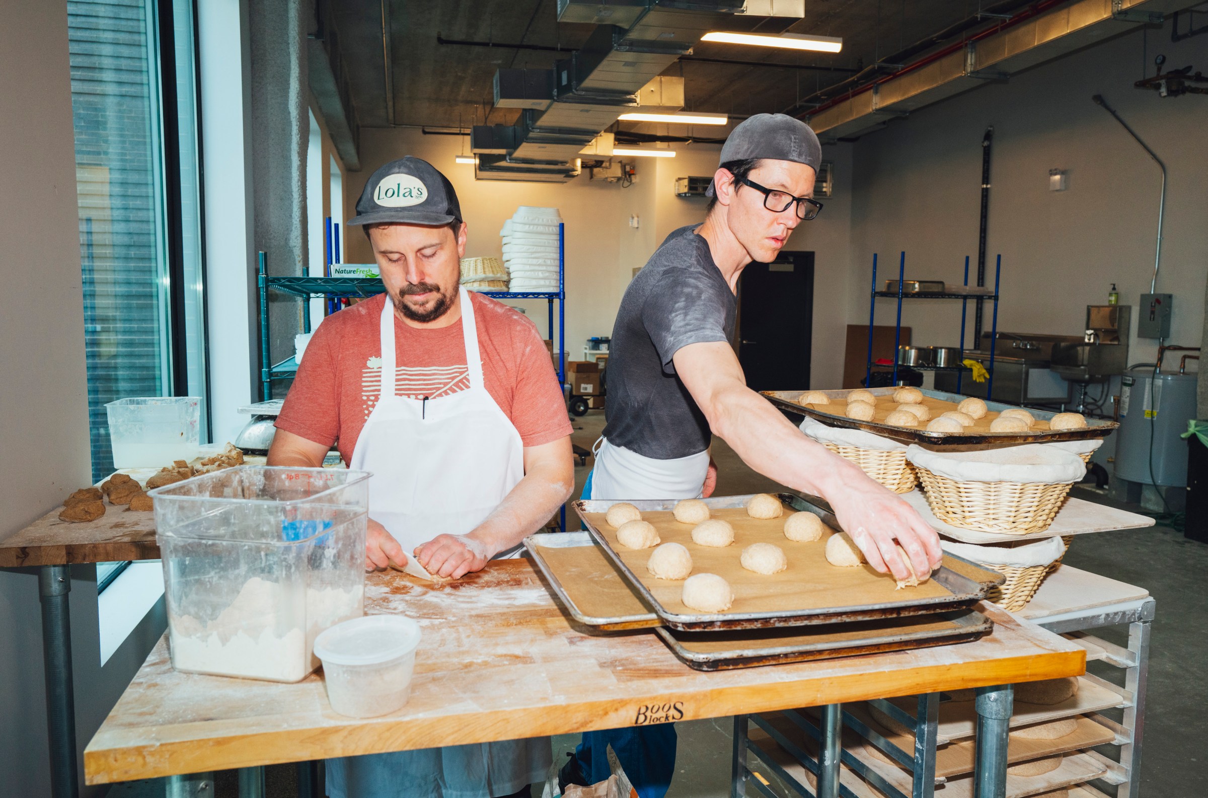 Two people prepping dough balls at a table.