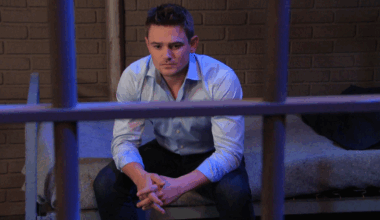 Days Johnny looks miserable as he sits on a bed in a jail cell, hands together, staring at nothing
