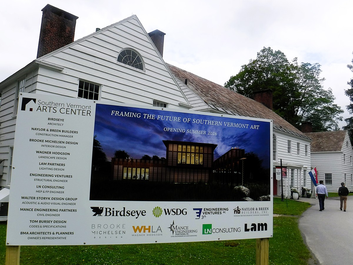 A large sign in front of white buildings displays information about the upcoming Southern Vermont Arts Center project, scheduled to open in summer 2026.