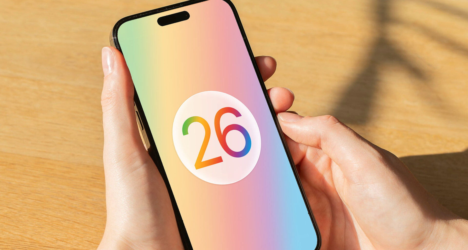 A render of the Apple iOS 26 logo on an iPhone held in a hand.