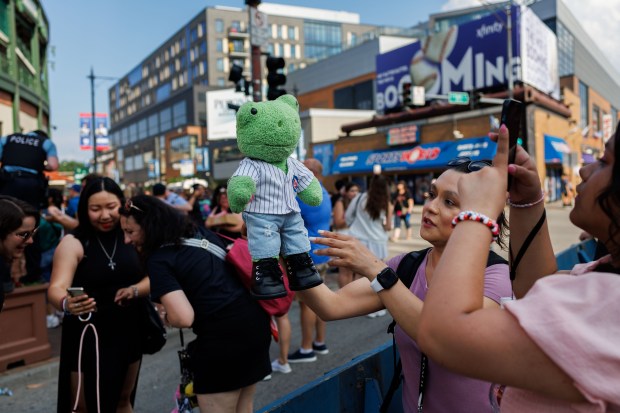 Mariela Castaneda holds Mr. Hoppers while her daughter Natalia Castaneda, 15, takes a photo of her stuffed frog outside Wrigley Field before the Stray Kids concert on June 26, 2025. (Armando L. Sanchez/Chicago Tribune)