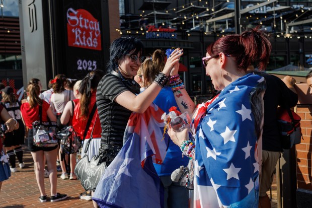 Onyx Dupree, 18, left, from Indiana, high-fives Erin Wiegand, 45, from Cleveland, while both wear flags with Stray Kids band member Bang Chan outside Wrigley Field, June 26, 2025, in Chicago. (Armando L. Sanchez/Chicago Tribune)