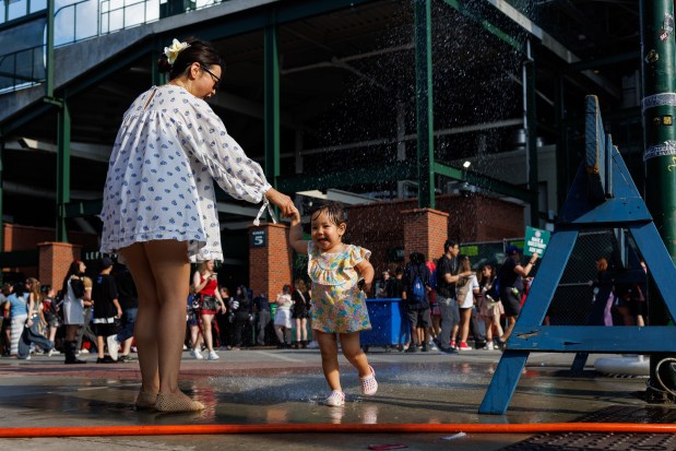 Manda Ganbaatar plays outside in a sprinkler with her daughter Mia Pirman, 2, outside before Stray Kids perform at Wrigley Field, June 26, 2025, in Chicago. (Armando L. Sanchez/Chicago Tribune)