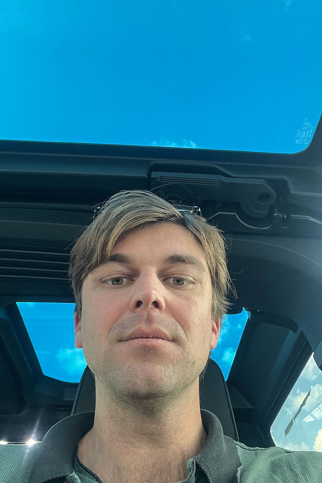 A blond man takes a selfie inside a car with a moonroof.
