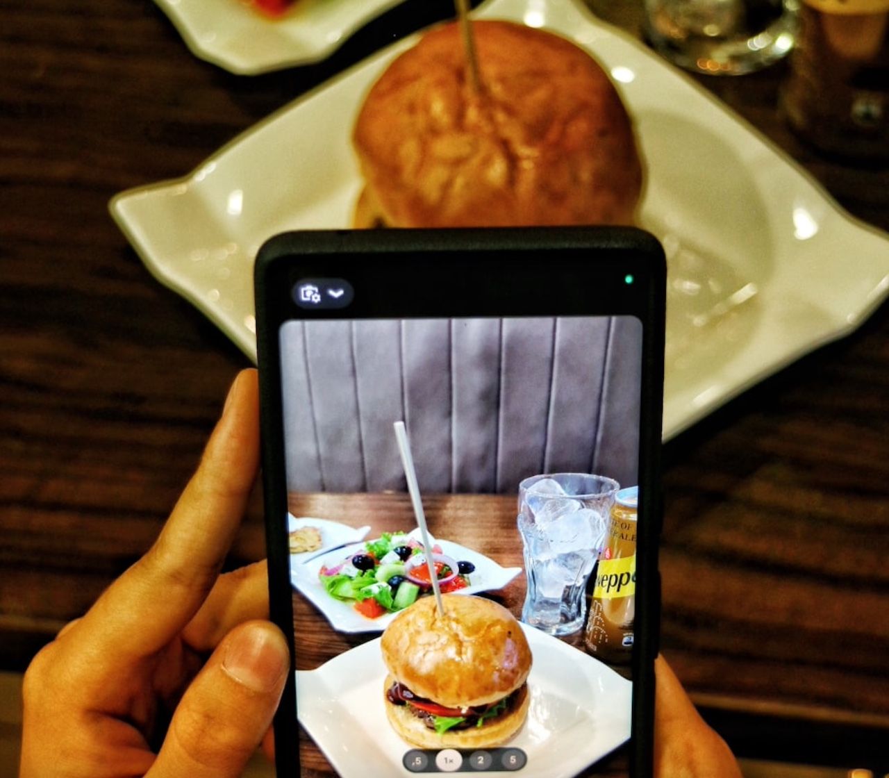 Hand holding phone and taking picture of burger and drinks on table