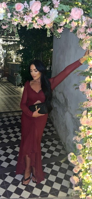 Woman in a burgundy dress posing under a floral archway.