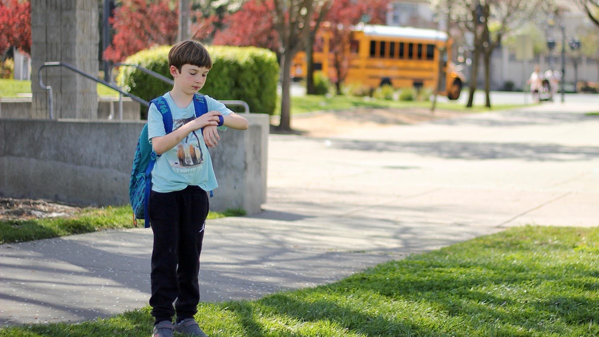 A child in front of a school looking at his smartwatch