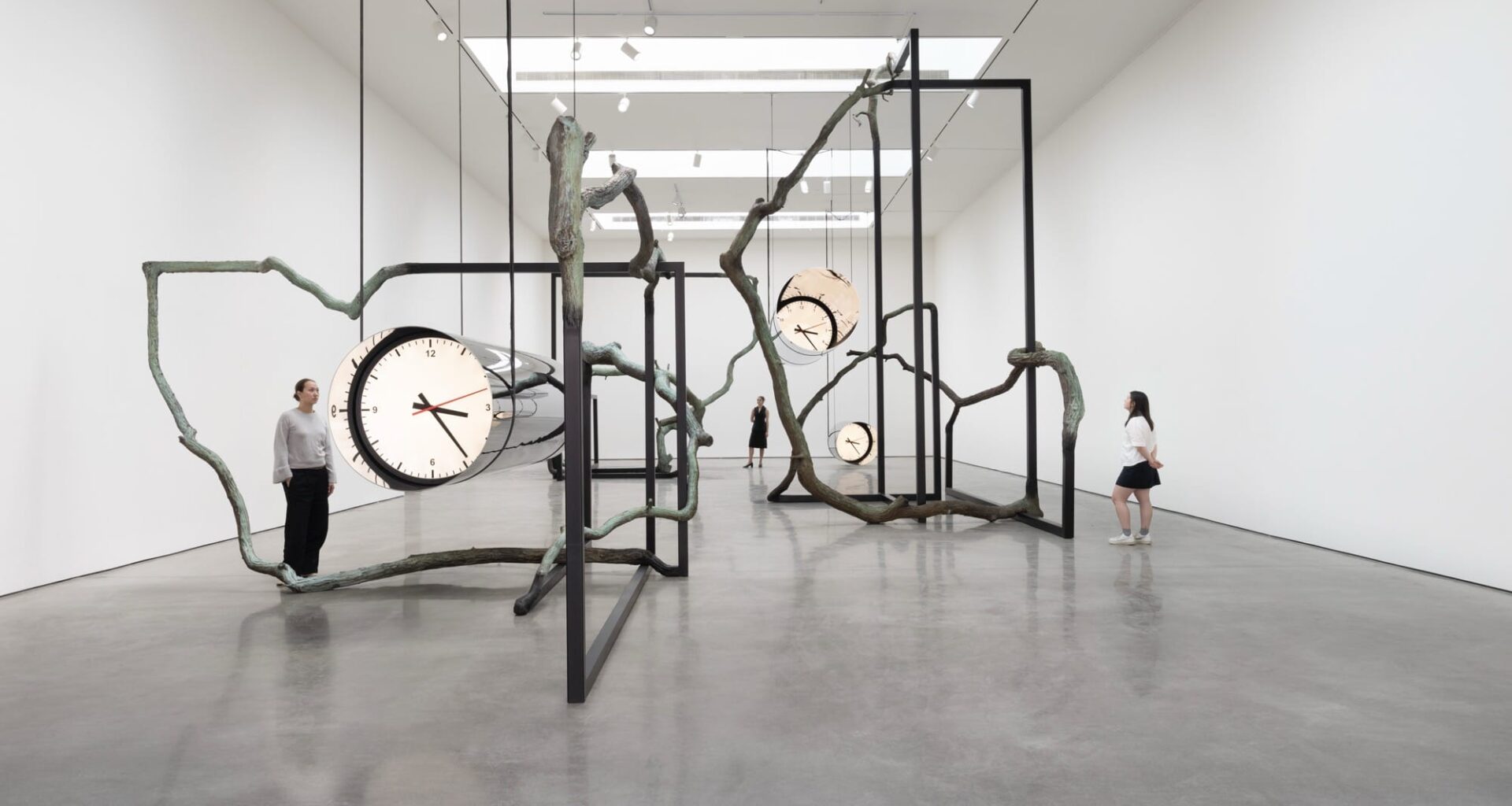 large suspended cylindrical metal sculptures with distorted clocks on the end suspend from a gnarled, tree like sculpture