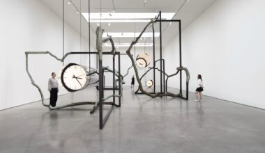 large suspended cylindrical metal sculptures with distorted clocks on the end suspend from a gnarled, tree like sculpture