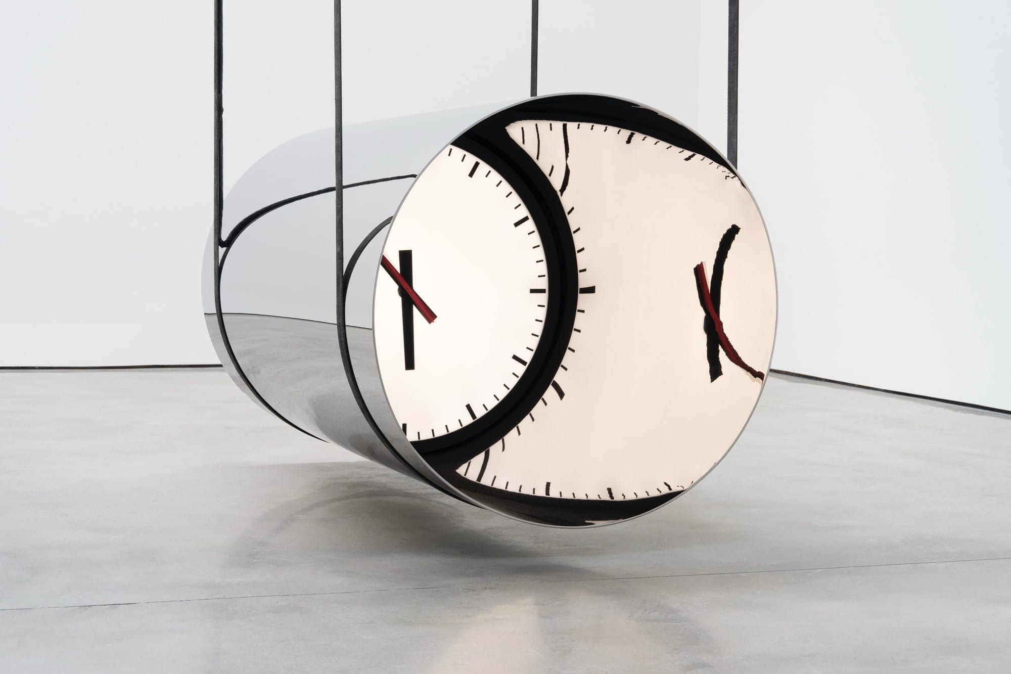 a large suspended cylindrical metal sculpture with a distorted clock on the end