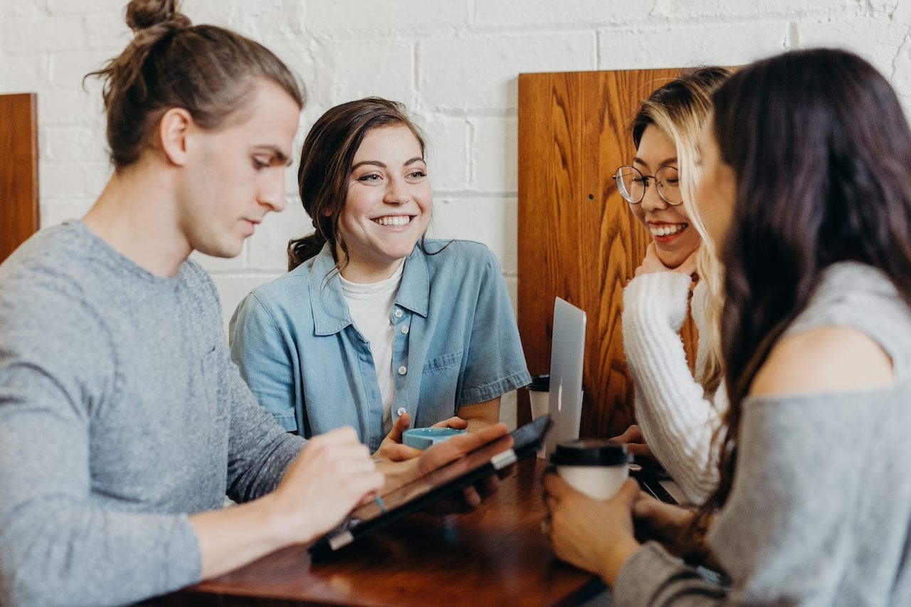 Man using tablet while three ladies laugh and talk beside him