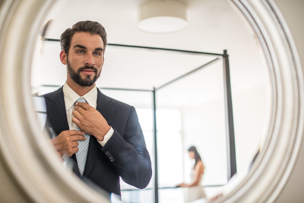 mirror reflection of young businessman adjusting shirt and tie in hotel room, dubai, united arab emirates