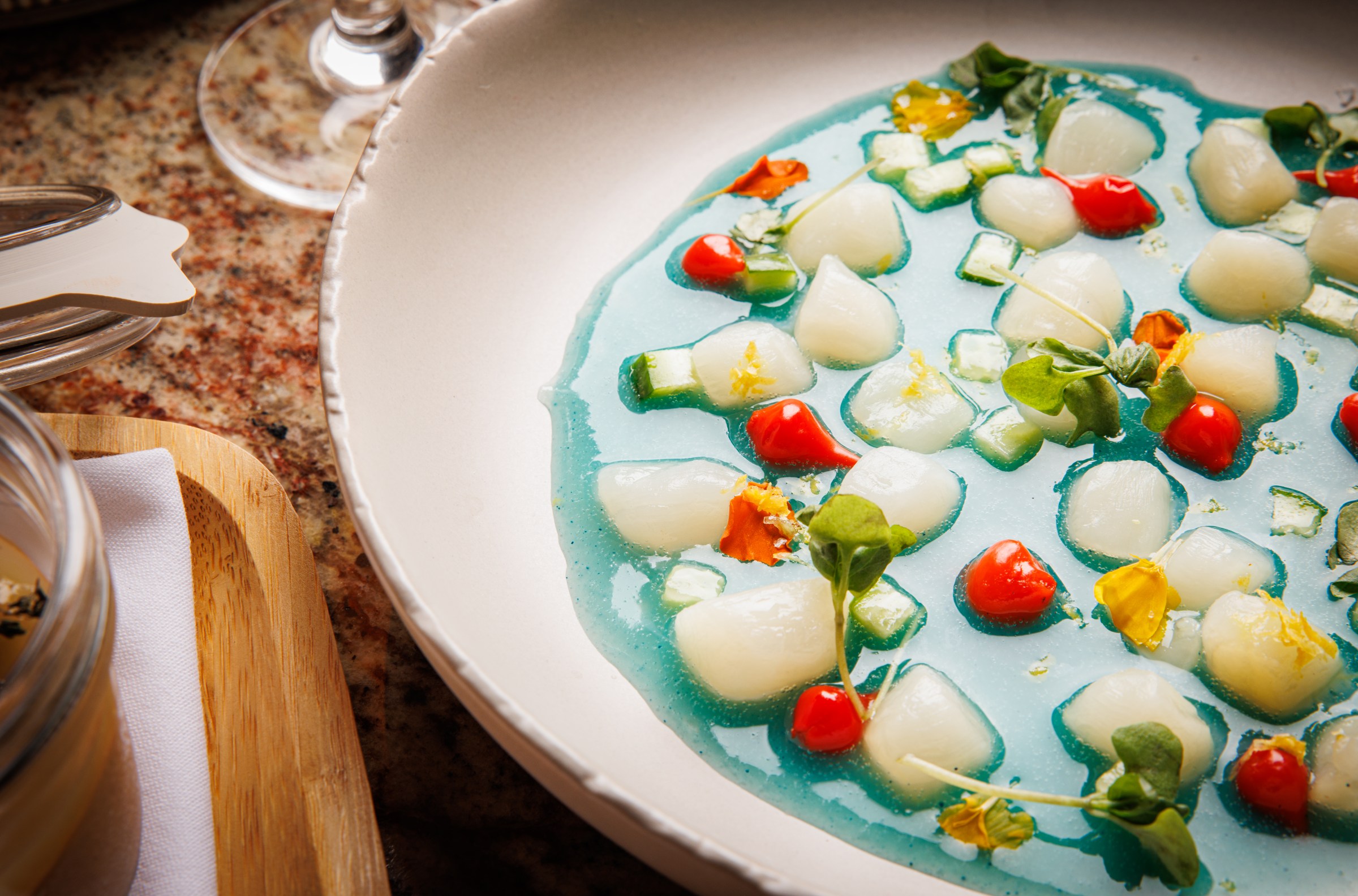 A bowl of scallop crudo in blue sauce.