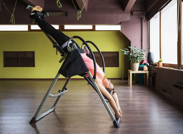 A woman doing inversion therapy hanging upside down on an inversion table, the therapy session is being done in a studio