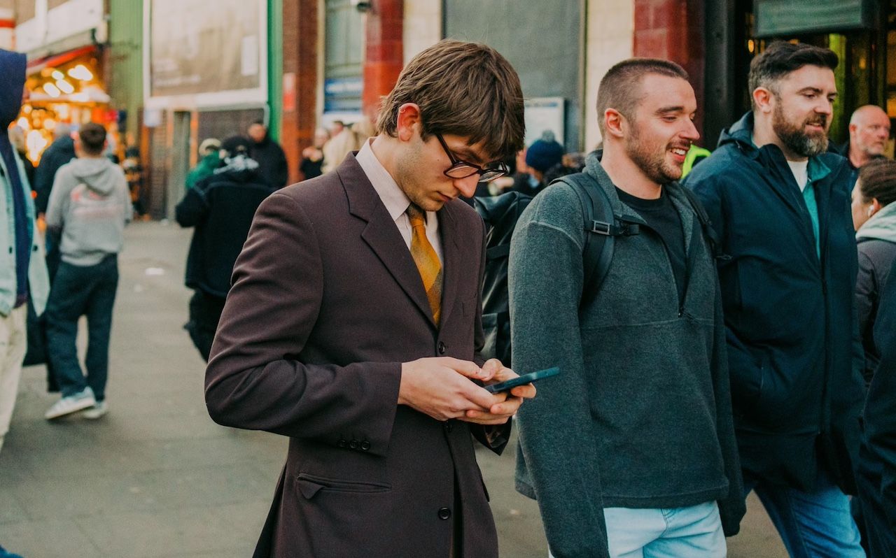 Man in formal outfit using phone in crowded street