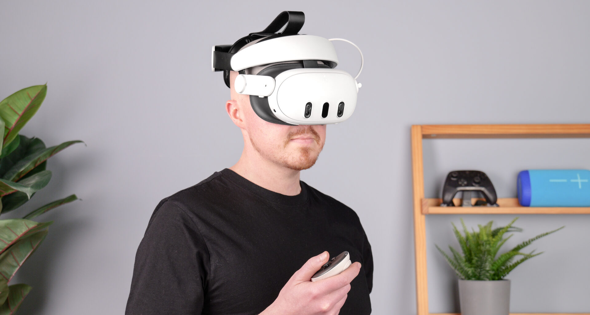 Kiwi Design H4 Boost Halo Battery Strap with Meta Quest 3 on person holding controller and plant and shelf in background