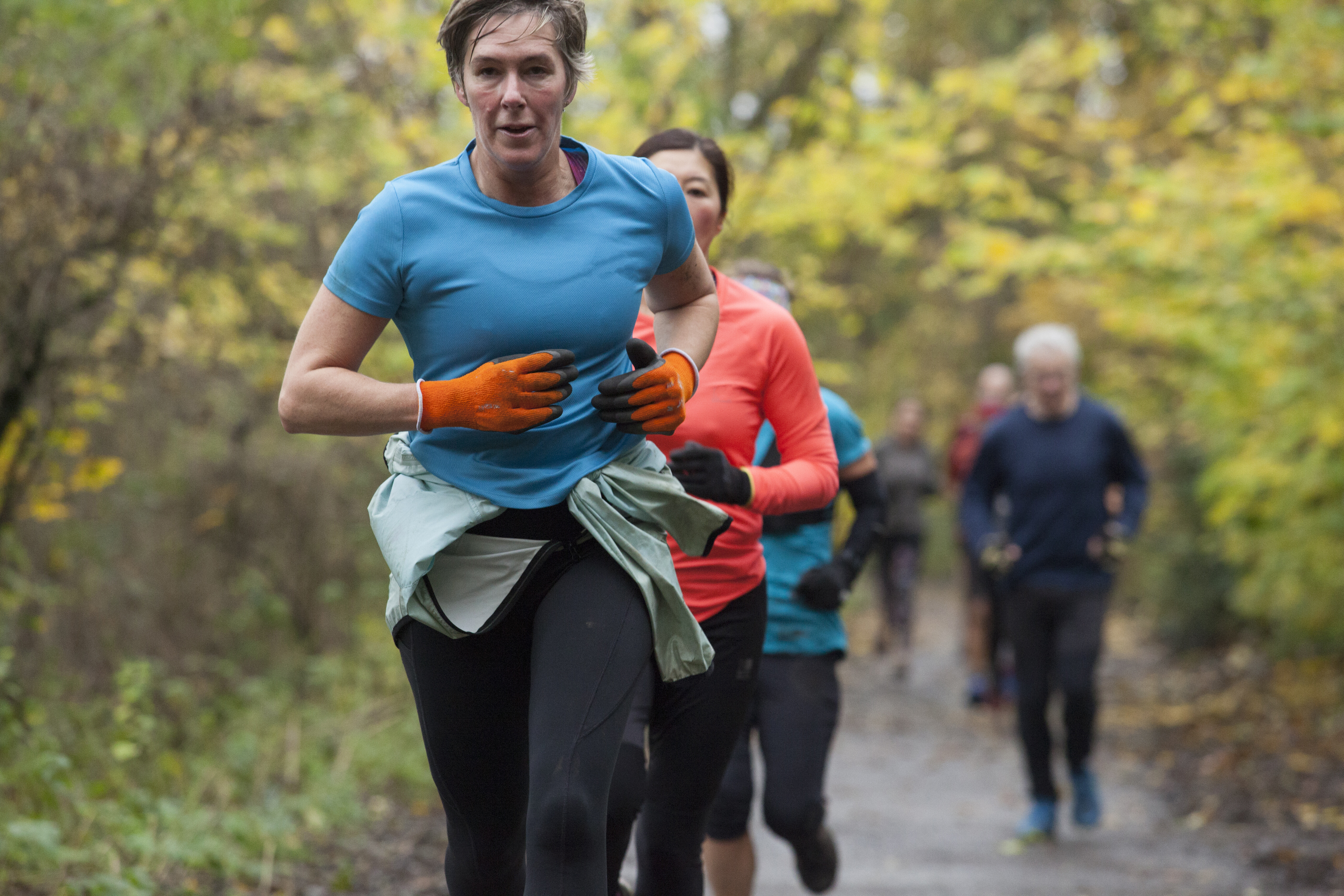 A group of adults jogging on a leaf-strewn trail in autumn.