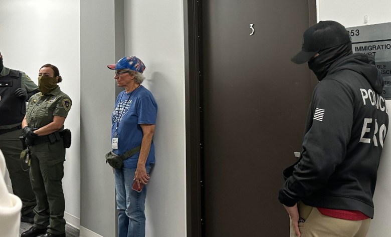 There's a lot of waiting in immigration court between arrests. Here, volunteer Nancy Francis, stands against the wall with uniformed federal officers. 