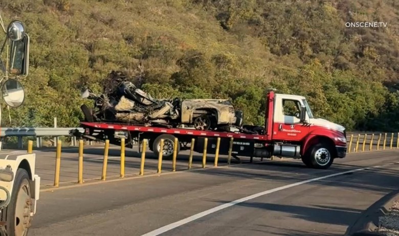 A tow truck on state Route 67 carts away part of the burned wreckage after Friday's fatal collision.