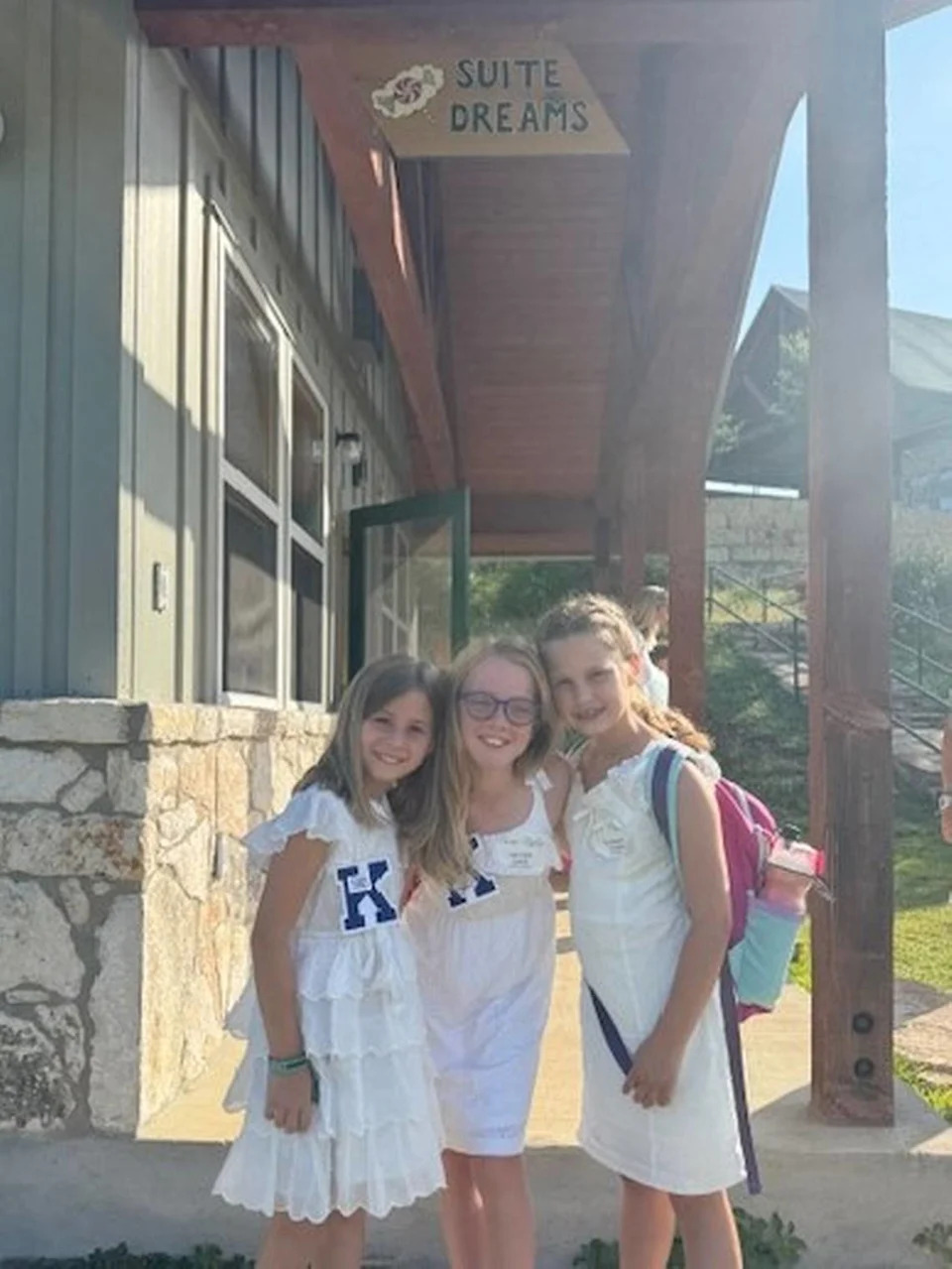 Binney Gilpin, 8; Corrigan Camp, 9; and Elizabeth Arnold, 8, pose in front of a cabin at Camp Mystic in June 2025.