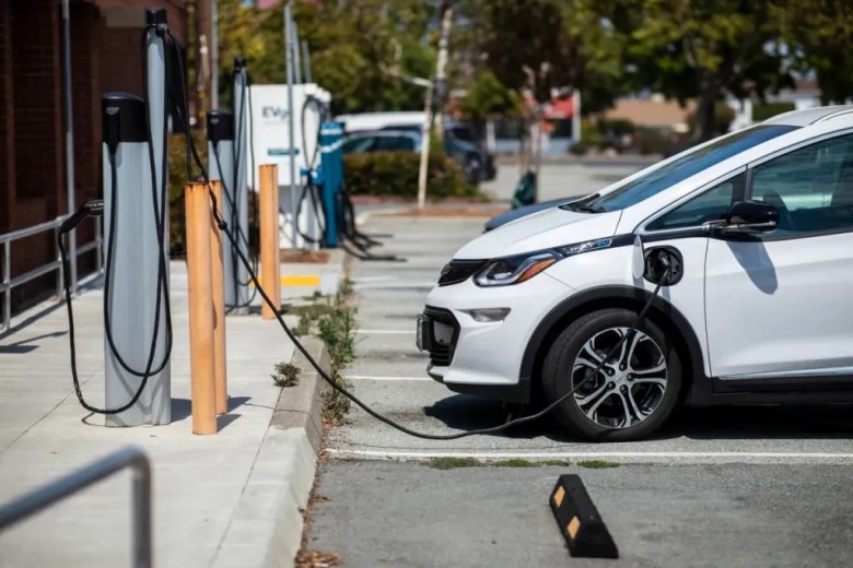 A white electric car charging in a parking lot with several charging stations.