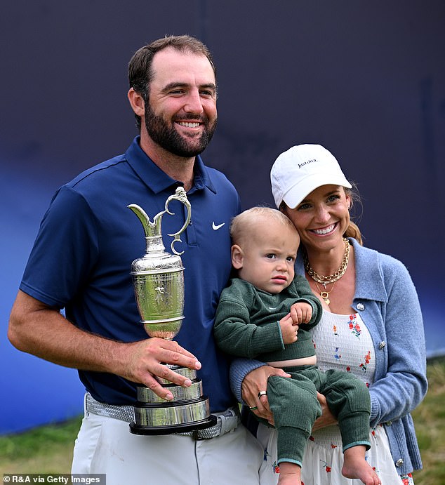 : Scottie Scheffler of the United States lifts the Claret Jug on the 18th green alongside his wife Meredith Scheffler and son Bennett Scheffler following his latest major victory