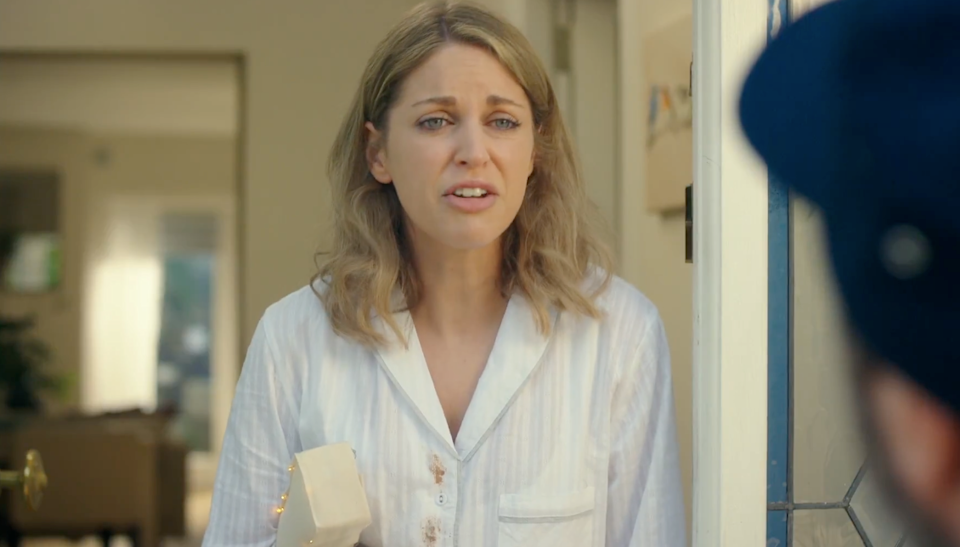 Woman in pajamas holds a phone at the door, looking concerned, engaging with an unseen person outside