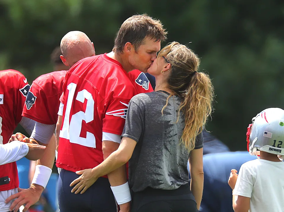 A football player in uniform kisses a woman on a field with others nearby