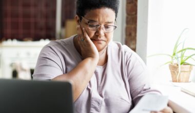 A mature African American woman in glasses touches her cheek, looking sad and puzzled by a high utility bill.