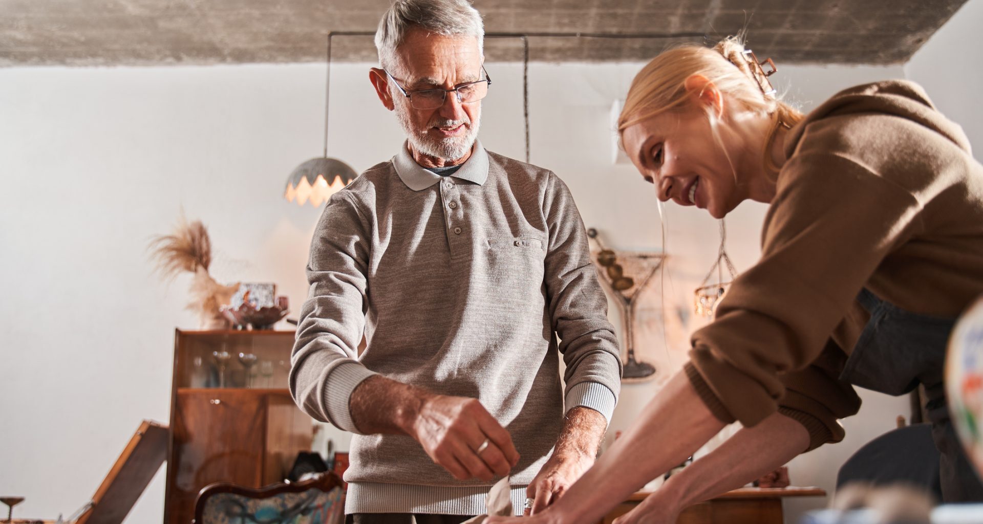 Low angle view of the cheerful blonde woman packing ceramic dishes at the craft paper and boxes and smiling.