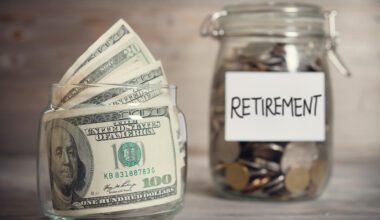 A jar of $100 dollar bills next to a jar of coins labeled